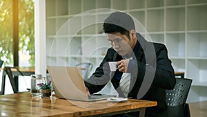 A young Asian businessman who works in front of a laptop and drinks coffee to cure sleepiness in his photo