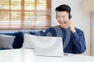 Young asian businessman working on laptop computer wearing headphone at home.