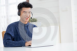 Young asian businessman working on laptop computer wearing headphone at home.