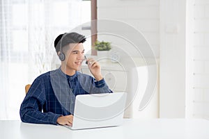 Young asian businessman working on laptop computer wearing headphone at home.