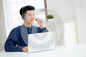 Young asian businessman working on laptop computer wearing headphone at home/