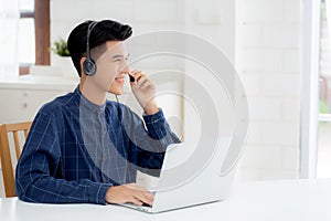 Young asian businessman working on laptop computer wearing headphone at home.