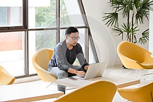 Young Asian businessman working on laptop in modern office.