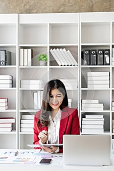 Young Asian businesswoman is happy to work at the modern office using a tablet and laptop