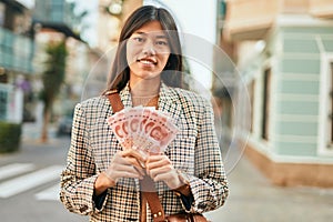 Young asian businesswoman smiling happy holding chinese yuan banknotes at the city
