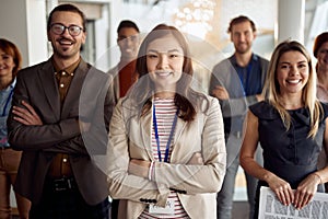 Young asian businesswoman, standing in front of her team. arms crossed, smiling, looking at camera, eye contact. bold and outgoing