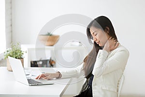 Young asian businesswoman feels neck pain after sedentary comput photo