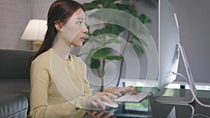 Young Asian businesswoman working from home and typing using desktop computer in living room