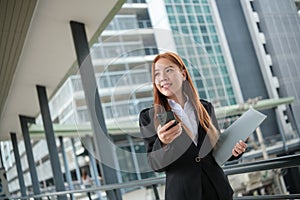 A young Asian businesswomen wearing a suit holding files standing in a big city on a busy downtown street. Young Asian