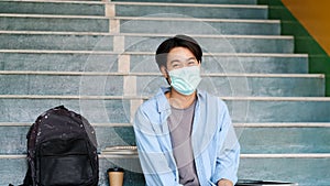 Young asian campus student man wearing protection mask smiling and looking at camerawhile sitting in campus, coronavirus