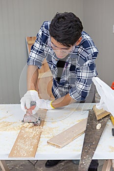 Young asian carpenter holding sanding machine polishing on wooden job