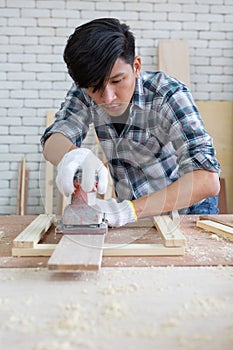 Young asian carpenter polishing wooden job with sanding machine