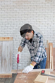 Young asian carpenter sawing wooden job with handsaw