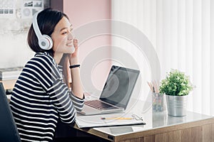 Young asian casual businesswoman arm on desk rest pose with laptop computer and listening music via headphone and looking through