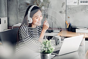 Young asian casual businesswoman arm on desk rest pose with laptop computer and listening music via headphone and think about