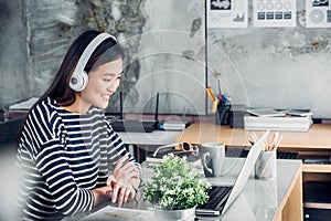 Young asian casual businesswoman arm on desk rest pose with laptop computer and listening music via headphone and think about