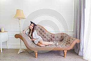 Young asian cat woman is lying on a couch in modern room