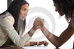 Young asian and caucasian businesswomen armwrestling struggle for leadership