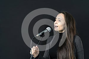 Young Asian or Caucasian woman holding mic, singing song alone in music studio