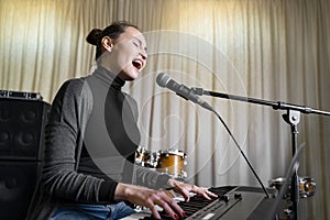 Young Asian or Caucasian woman singing song loud on mic, playing electro piano