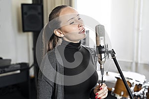 Young Asian or Caucasian woman singing to microphone in music or radio studio
