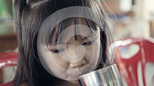 Young Asian child drinking a glass of water .