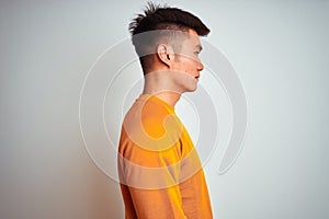 Young asian chinese man wearing orange sweater standing over isolated white background looking to side, relax profile pose with