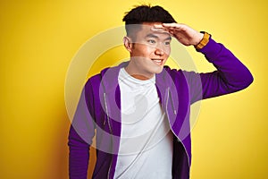 Young asian chinese man wearing purple sweatshirt standing over isolated yellow background very happy and smiling looking far away