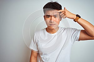 Young asian chinese man wearing t-shirt standing over isolated white background pointing unhappy to pimple on forehead, ugly