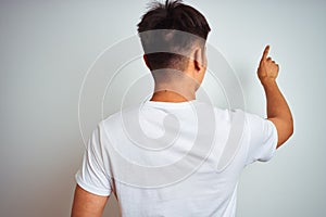 Young asian chinese man wearing t-shirt standing over isolated white background Posing backwards pointing ahead with finger hand