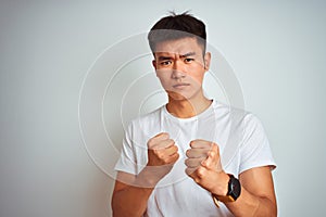 Young asian chinese man wearing t-shirt standing over isolated white background Ready to fight with fist defense gesture, angry