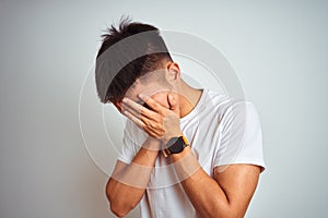 Young asian chinese man wearing t-shirt standing over isolated white background with sad expression covering face with hands while