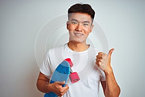 Young asian chinese student man holding skate standing over isolated white background happy with big smile doing ok sign, thumb up