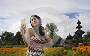 Young Asian Chinese tourist woman taking self portrait selfie photo with mobile phone on excursion through beautiful flowers field