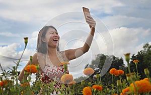 Young Asian Chinese tourist woman taking self portrait selfie photo with mobile phone on excursion through beautiful flowers field