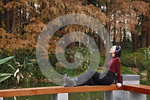 Young asian chinese woman listening to music with headphones sit under tree