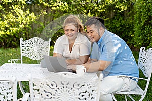 Young Asian chubby couple using a laptop in the outdoors green park together. Happy smiling man and woman working