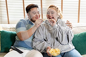 Young Asian chubby couple watching tv series and movie on the couch in living room. Man and woman enjoying a fun time