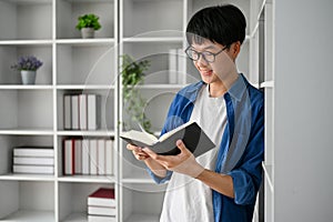 Young Asian college student with glasses reading book in the study room