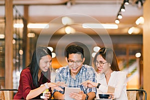 Young Asian college students or coworkers using digital tablet together at coffee shop, diverse group. Casual business, freelance