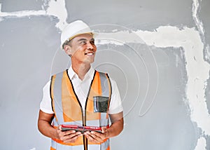 A young Asian construction worker looks to the right in front of cracked wall
