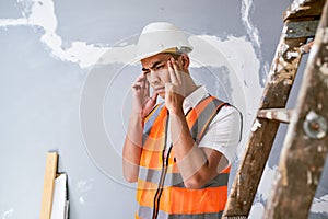 A young Asian construction worker rubs his temples in pain on site