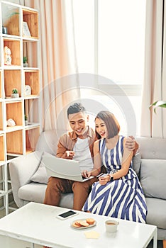 Young Asian couple buying online or paying bills by credit card with laptop at home