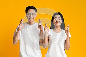 Young asian couple closing eyes and crossing fingers with hope