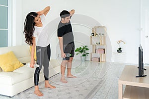 Young Asian couple doing High-intensity interval training together and looking TV at home, man and woman working out together