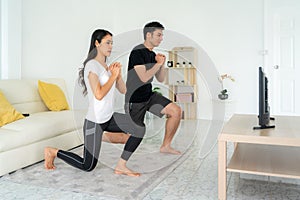Young Asian couple doing squats training together and looking TV at home, man and woman working out together standing in living