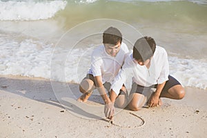 Young asian couple gay smiling romantic drawing heart shape together on sand in vacation