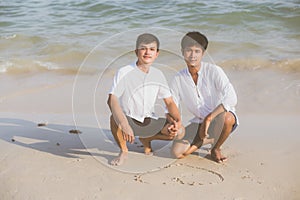 Young asian couple gay smiling romantic drawing heart shape together on sand in vacation