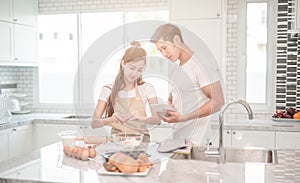 Young asian couple happy make bakers helping to make bakery see recipes form tablet.