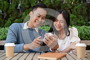 Young Asian couple listening to music together, having fun together in the green park